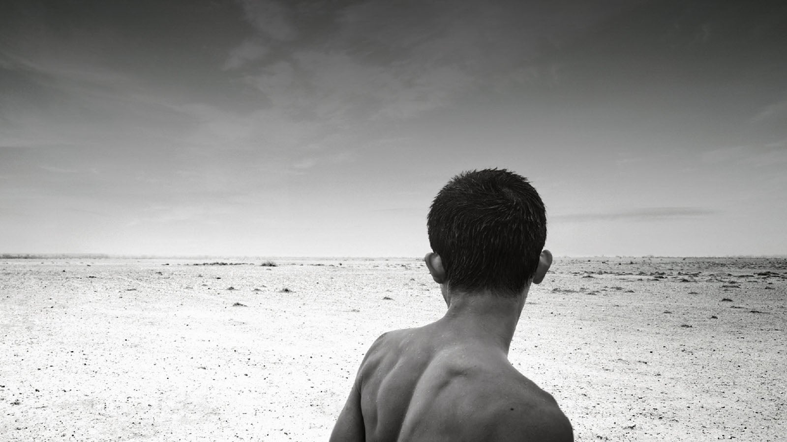 Black and white photo of a young boy looking out over a vast barren landscape